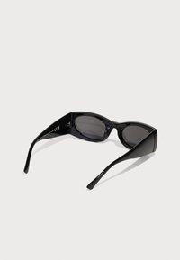 Occhiali da sole neri con un design elegante e angolare, lenti scure e montatura in plastica lucida. Aste sottili che si assottigliano verso le punte.