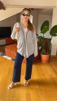 Grå, överdimensionerad cardigan med svart kant och en knapp, i kombination med blå vida byxor och vita klacksandaler. Tillbehör inkluderar solglasögon.