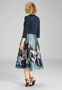 Vestido de estampado floral con un cuerpo ajustado en azul marino y una falda fluida en teal. Presenta mangas de 3/4 y detalles plisados.