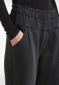 Joggers in denim nero con una vita elasticizzata e tasche laterali. Presentano pieghe sul davanti e una finitura morbida e texturizzata.