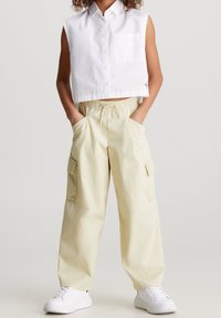 Vit, kortärmad och ärmlös skjorta med en framficka, tillsammans med beige cargobyxor med sidofickor, bärs med vita sneakers.