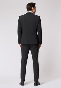 Completo nero su misura con una vestibilità strutturata. Presenta un colletto a scollatura, una fessura singola e pantaloni dritti. Tessuto semplice con dettagli in bottone.