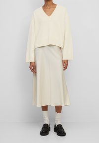 Pull col en V crème avec ourlet côtelé et manches surdimensionnées, associé à une jupe midi fluide crème et des mocassins noirs épais.