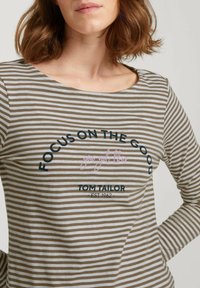 Maglietta a maniche lunghe a righe in marrone e beige, con scollatura rotonda. La scritta include "FOCUS ON THE GOOD" e il nome del brand "TOM TAILOR."