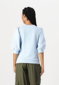 Sweatshirt azul claro com mangas bufantes, gola redonda e punhos canelados. Textura de tecido suave; combinado com calças cargo verde exército.