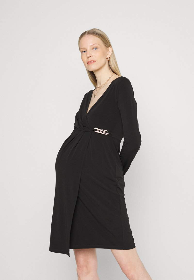 Vestido preto envolvente feito de tecido suave, com mangas longas, um decote em V profundo e um detalhe torcido na cintura com realces de corrente metálica.