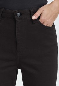 Vaqueros negros de talle alto con una textura suave, que cuentan con un cierre de botón, bolsillos laterales y detalles cosidos a lo largo de las costuras.