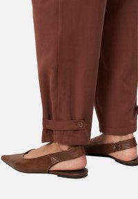 Pantalons marron, longueur cheville, avec des ourlets retroussés et des accents de boutons, associés à des flats en cuir marron à talon ouvert avec un bout pointu.