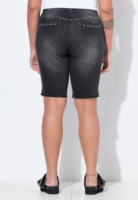 Sorte denim bermuda shorts med frynset kant, to baglommer og dekorative nitter på taljen. Glat overflade og tætsiddende design.
