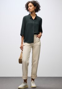 Mörkgrön kortärmad skortärmad skjorta, ljusbeige löst sittande byxor och vita sneakers. Utseendet kompletteras av en liten brun handväska.