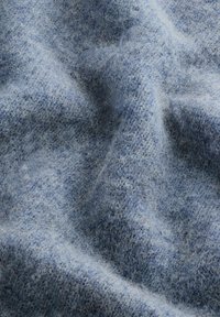 Un tissu bleu clair et doux avec un motif tricoté flou et texturé, dont les nuances variées créent une profondeur et une dimension subtiles.