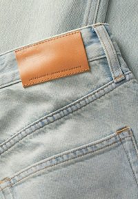 Világoskék farmer overall, barna bőrpólóval ellátva, amelyen "JACK & JONES / JEANS INTELLIGENCE" felirat található. Látható varrásokkal és zsebekkel rendelkezik.