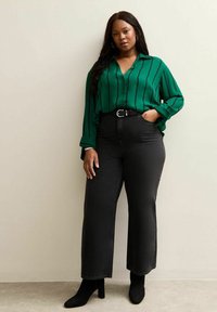 Blouse à rayures vertes avec un design à boutons, associée à un jean noir taille haute et des bottines noires. Tissu lisse avec une coupe décontractée.