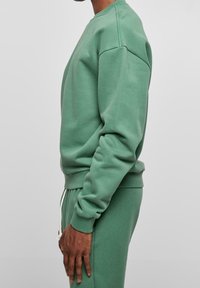 Sweat-shirt vert en mélange de coton, avec un col rond, des poignets et un ourlet côtelés, et une coupe décontractée. Porté avec un pantalon de survêtement assorti.