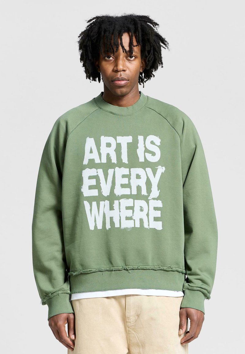 Felpa verde con collo a giro, maniche raglan e orlo sfrangiato. Testo "L'ARTE È OVUNQUE" in bianco, carattere in grassetto sul fronte.