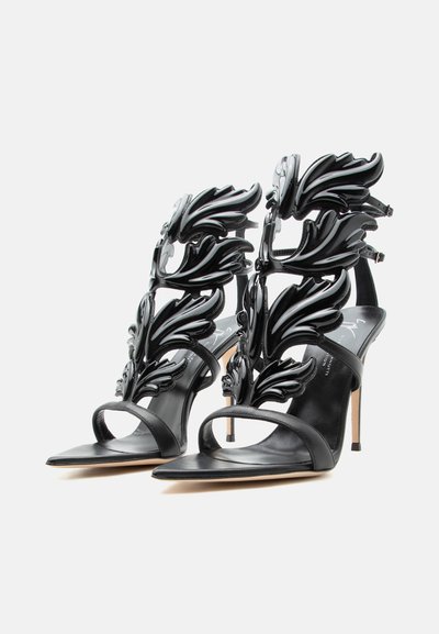 Μαύρα πέδιλα με ψηλό τακούνι, μυτερά δάχτυλα, λουράκια στον αστράγαλο και διακοσμητικά γυαλιστερά ανάγλυφα σχέδια σε σχήμα φύλλων στο πάνω μέρος.