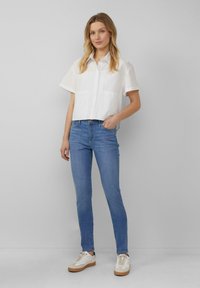 Chemise blanche à manches courtes avec un devant à boutons, associée à un jean skinny bleu clair et des baskets blanches avec des accents beige.
