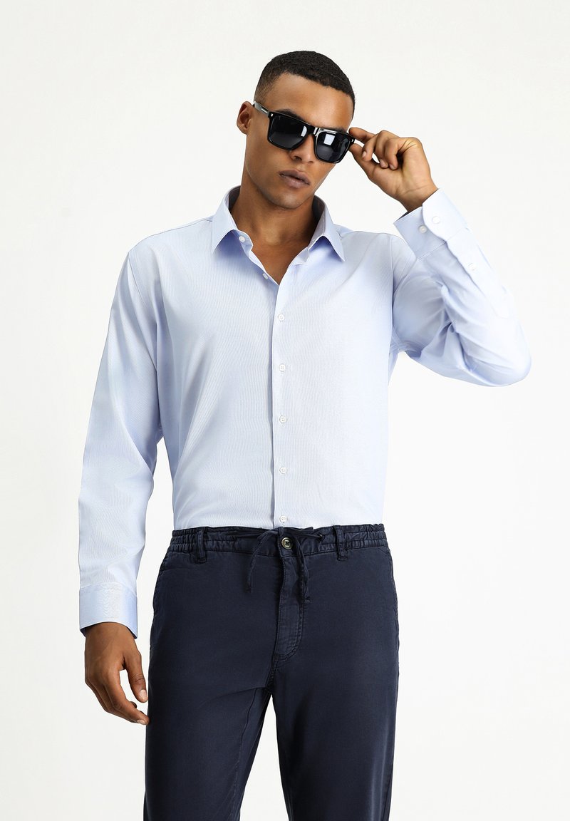 Jasnoniebieska koszula z długim rękawem o paskowanej teksturze, z kołnierzykiem zapinanym na guziki, zestawiona z granatowymi spodniami z elastycznym paskiem i sznurkiem.