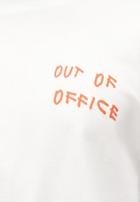 Λευκό ύφασμα με πορτοκαλί κείμενο που γράφει «ΕΚΤΟΣ ΓΡΑΦΕΙΟΥ» σε έναν χαλαρό, χειροποίητο στιλ.