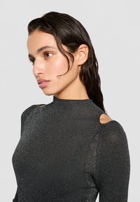 Top nero a maniche lunghe realizzato in un tessuto testurizzato e scintillante. Caratterizzato da un collo alto e aperture sulle spalle per un tocco di dettaglio.