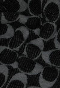 Vilnonis audinys su pilku fonu, dideliais juodais taškiais ir tekstūruotomis juodomis juostelėmis, sukuriantis sluoksniuoto rašto efektą.