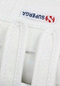 Baskets blanches avec une surface texturée et brillante. Design à lacets avec des lacets plats blancs et une étiquette de logo visible pour Superga.