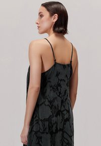 Czarna i szara sukienka w marmurkowy wzór, z cienkimi regulowanymi ramiączkami i luźnym, zwiewnym krojem. Miękka faktura materiału.