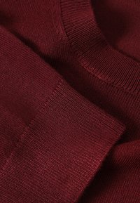 Gros plan sur un pull tricoté bordeaux plié montrant les détails du col et des poignets côtelés.