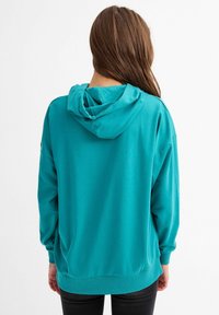 Sudadera con capucha en color teal, de manga larga, fabricada en un tejido suave, con un corte relajado, puños y dobladillo acanalados, y con capucha ajustable mediante cordones.