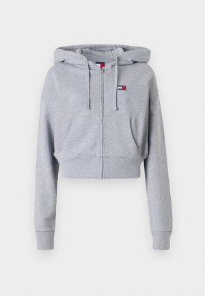 Grå kort hoodie med glidelås foran, hette med snøre og to frontlommer. Har logo-patch i rødt, hvitt og blått på brystet.