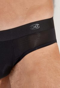 Schwarze Herrenunterwäsche mit glatter Textur und elastischem Bund, der ein dezentes Logo trägt. Der Stoff wirkt atmungsaktiv und formschlüpfrig.