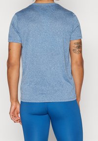 Blå, kortärmad träningsskjorta tillverkad av ett texturerat, fukttransporterande tyg. Bakifrån visas en slät design med en rundad fåll.