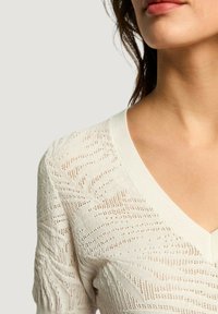 Maglione bianco lavorato a maglia con scollo a V, caratterizzato da motivi traforati intricati e dettagli a coste sulle maniche e sull'orlo.
