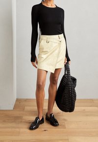 Haut noir à manches longues côtelé, jupe asymétrique métallique dorée, tissu texturé, chaussures plates noires, et un grand sac cabas tissé noir.