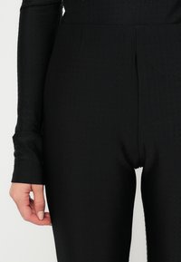 Must hemmed mustriga bodysuit, millel on tekstureeritud pind, kus on väiksed kõrgendatud täpid; keha kohandav disain, siledate kangastega, millel on kerge läige.