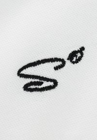 Weißer Stoff mit einem schwarzen gestickten Logo, das aus einem stilisierten "S" mit einem kleinen Akzentdetails in Form eines Blattes besteht.