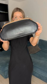 Pochette en cuir noir avec une monture et un fermoir en métal doré. Présente une forme arrondie et un logo embossé sur le devant.