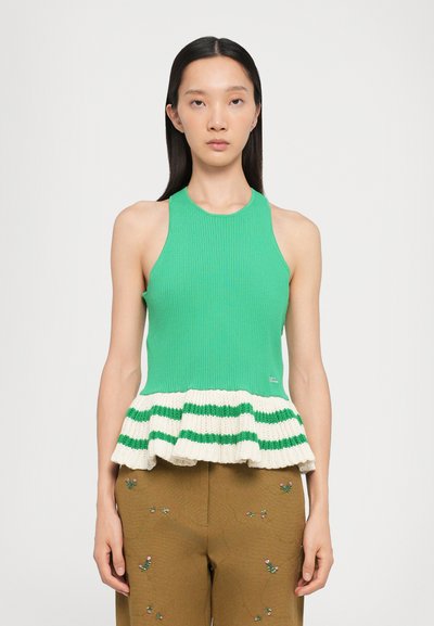 Haut halter vert à côtes avec un ourlet tricoté évasé présentant des rayures crème et vertes. Le modèle porte un pantalon brodé marron.