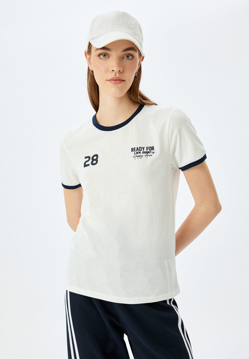 Hvid t-shirt med korte ærmer, navy krave og manchetter. Fås med trykt tekst og tallet "28" på brystet. Løs pasform, blødt materiale.