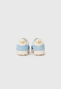 Baskets de sport en suède bleu avec des accents blancs et un logo embossé à l'arrière. Elles présentent une semelle texturée avec des clous visibles pour une meilleure adhérence.