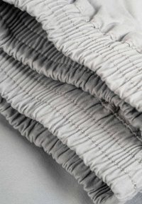 Tela gris con textura fruncida, que presenta tres filas de canales elásticos. Superficie lisa con un sutil brillo y finos detalles de costura.