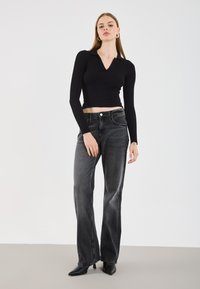 Black ribbed long-sleeve polo top paired with gray wide-leg jeans. Model wears black heeled shoes, with minimal accessories and a neutral backdrop.