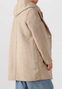 Beige wollen blend jas met een gestructureerde afwerking, voorzien van een capuchon, zijknopen en een relaxte pasvorm. Geaccentueerd met stiknaad langs de naden.