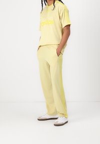 Ljusgul träningsoutfit med en kortärmad tröja med "adidas"-logotyp och matchande byxor med sidostripes och fickor.