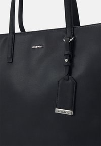 Borsa tote in pelle nera con una superficie liscia, con hardware argentato e un'etichetta con il marchio. Include manici lunghi per il trasporto.