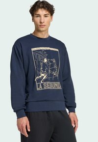 Sudadera azul marino de algodón con un estampado gráfico que muestra a dos jugadores de fútbol y el texto "LA SEGUNDA". Puños y dobladillo acanalados.