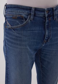 Blaue Jeans aus Denim mit geradem Schnitt, leicht ausgewaschen, mit Fronttaschen und Metallknopfverschluss. Nähte in kontrastierender Farbe.
