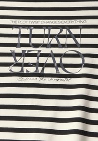 Stribet stof t-shirt i sort og hvid. Har en fed tekstgrafik: "TURN OVER" og mindre tekst "Embrace the Unexpected" trykt i grå.