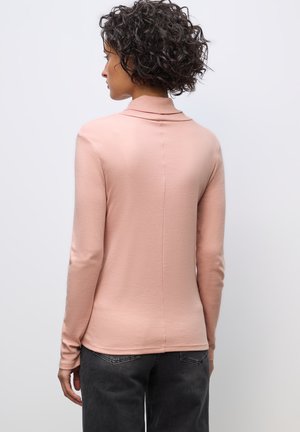 Lyserød langærmet top med foldet krave, lavet af blødt materiale, med et sømløst bagdesign og tætsiddende silhuet. Bæret med mørke jeans.