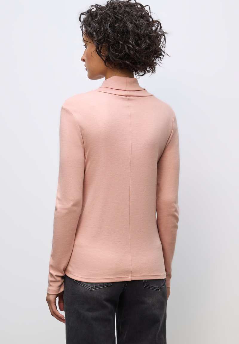 Lichtroze langärmelig shirt met een omgeslagen kraag, gemaakt van zacht materiaal, met een naadloos ontwerp aan de achterkant en een aansluitende silhouette. Draagt met donkerblauwe spijkerbroek.